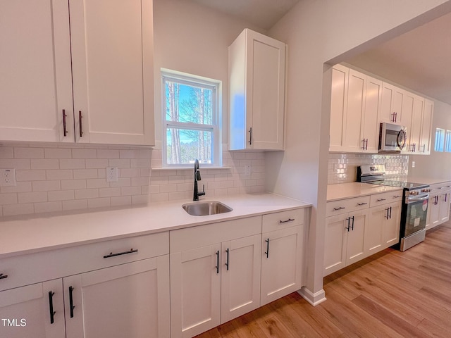 kitchen with sink, white cabinetry, light hardwood / wood-style flooring, stainless steel appliances, and decorative backsplash