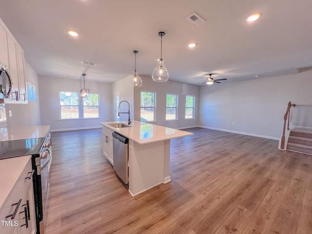 kitchen with appliances with stainless steel finishes, pendant lighting, sink, white cabinets, and a kitchen island with sink