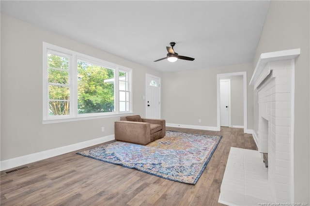 living room featuring ceiling fan, wood-type flooring, and a brick fireplace