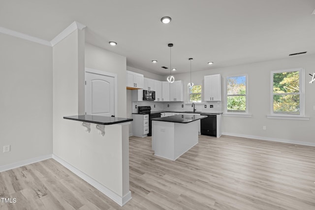 kitchen featuring white cabinetry, black appliances, hanging light fixtures, and light wood-type flooring