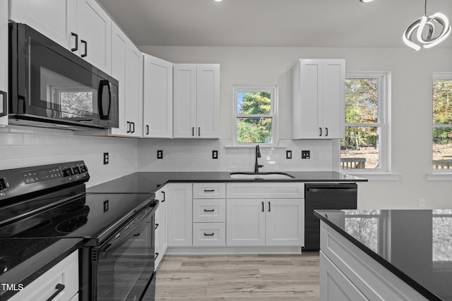 kitchen with hanging light fixtures, white cabinetry, black appliances, light hardwood / wood-style floors, and sink