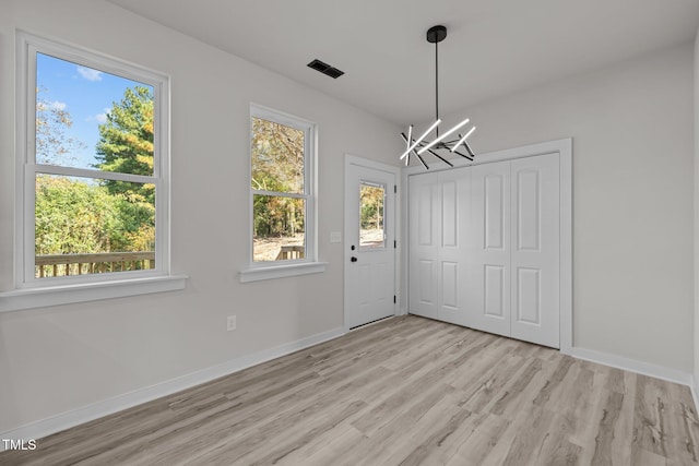 unfurnished dining area with an inviting chandelier and light hardwood / wood-style flooring