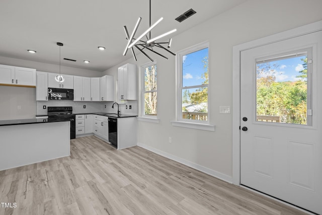 kitchen with white cabinetry, black appliances, hanging light fixtures, and a wealth of natural light