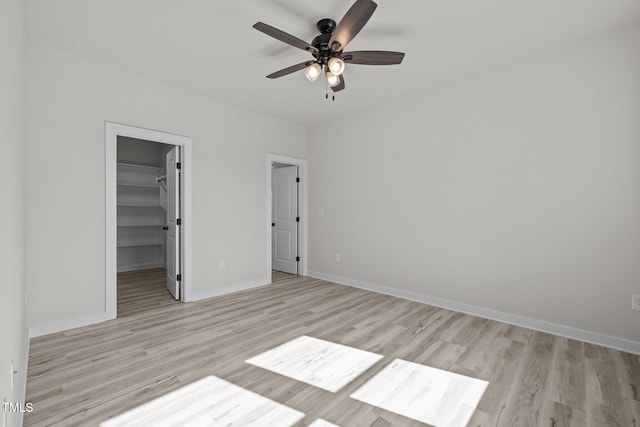 unfurnished bedroom featuring a closet, ceiling fan, light wood-type flooring, and a walk in closet