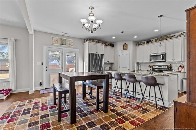 kitchen featuring a breakfast bar area, hanging light fixtures, a center island with sink, white cabinetry, and appliances with stainless steel finishes