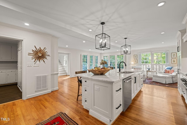 kitchen featuring light hardwood / wood-style flooring, a center island with sink, sink, pendant lighting, and stainless steel dishwasher