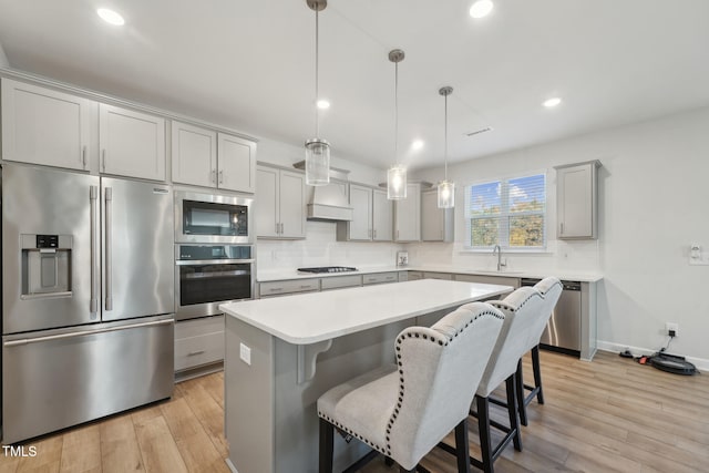 kitchen featuring stainless steel appliances, hanging light fixtures, sink, a kitchen island, and light hardwood / wood-style flooring