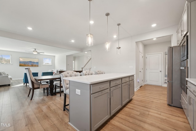 kitchen featuring light hardwood / wood-style floors, ceiling fan, a breakfast bar area, decorative light fixtures, and gray cabinetry