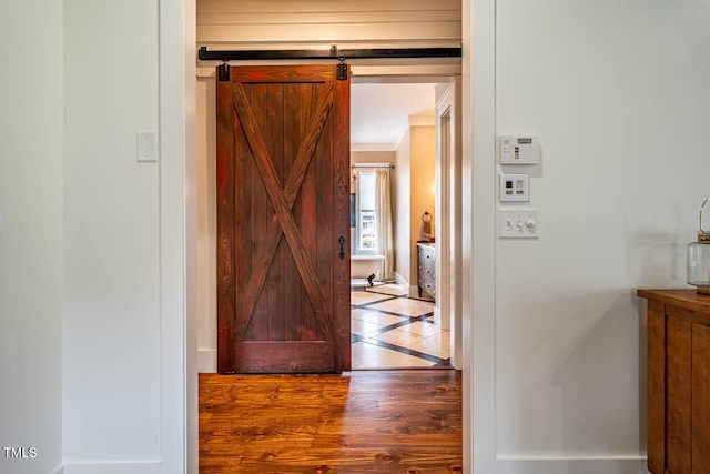 hall featuring wood-type flooring, ornamental molding, and a barn door