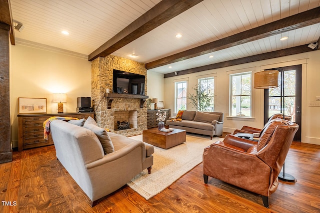 living room with beamed ceiling, wood-type flooring, a stone fireplace, and wooden ceiling