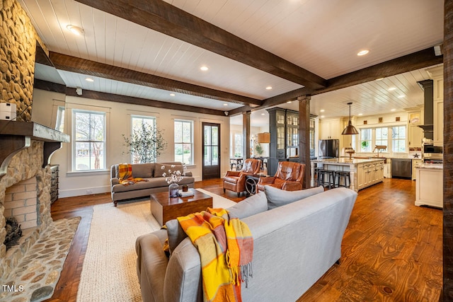 living room featuring ornate columns, a stone fireplace, a wealth of natural light, beamed ceiling, and dark hardwood / wood-style flooring