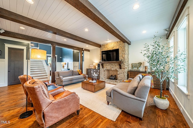 living room featuring beamed ceiling, a stone fireplace, and hardwood / wood-style floors