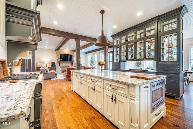 kitchen with a kitchen island, appliances with stainless steel finishes, decorative light fixtures, beamed ceiling, and a large fireplace