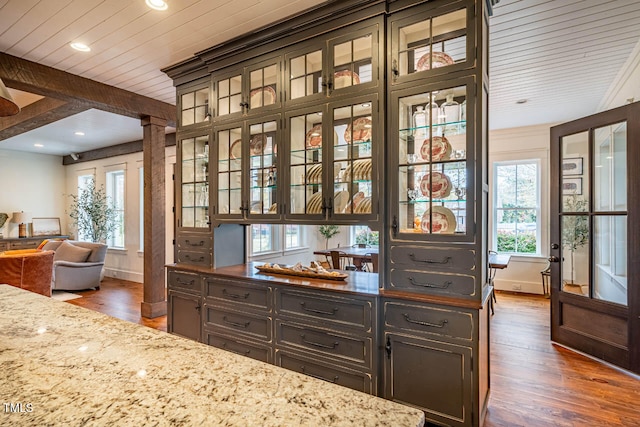 bar with light stone counters, dark hardwood / wood-style floors, decorative columns, and beam ceiling