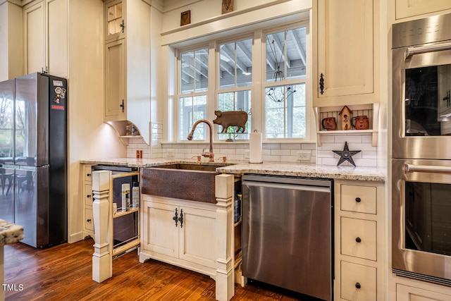 kitchen featuring appliances with stainless steel finishes, dark hardwood / wood-style floors, tasteful backsplash, sink, and light stone counters