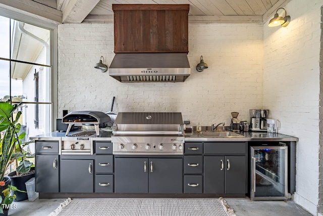 kitchen featuring gray cabinetry, beverage cooler, custom range hood, and brick wall