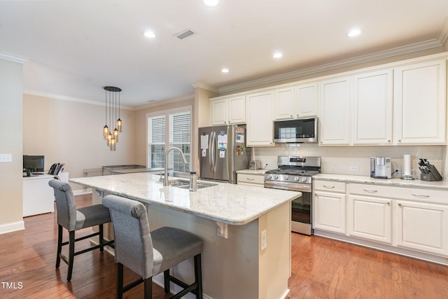 kitchen featuring hanging light fixtures, appliances with stainless steel finishes, a kitchen island with sink, light wood-type flooring, and sink