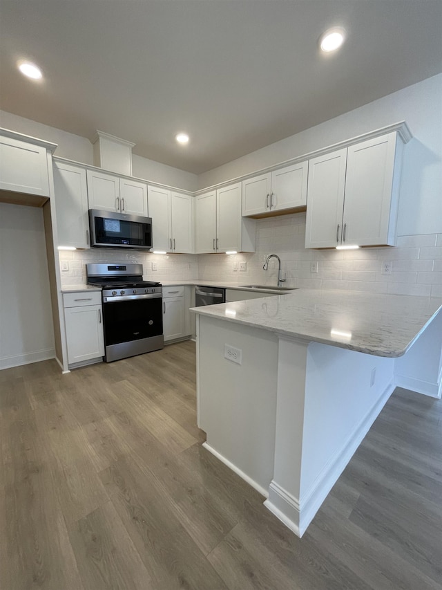 kitchen featuring sink, hardwood / wood-style flooring, decorative backsplash, appliances with stainless steel finishes, and white cabinetry