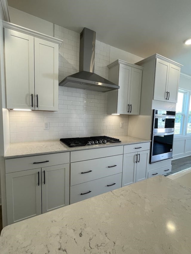 kitchen with wall chimney exhaust hood, appliances with stainless steel finishes, decorative backsplash, and white cabinets