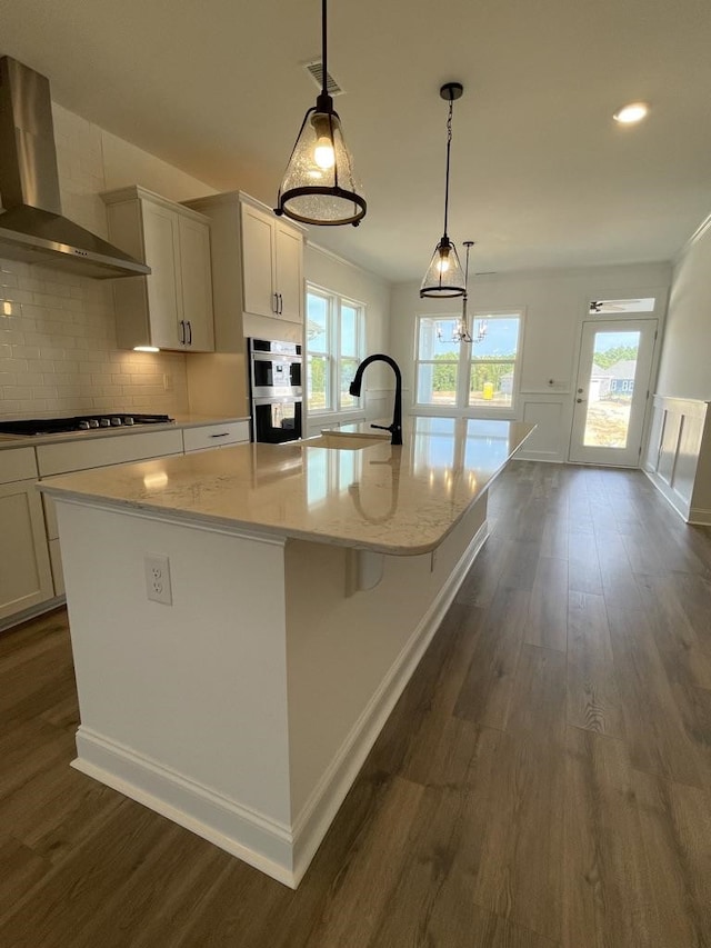 kitchen with wall chimney range hood, a large island, dark hardwood / wood-style floors, pendant lighting, and gas cooktop