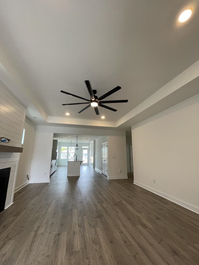 unfurnished living room featuring dark hardwood / wood-style floors, ceiling fan, a large fireplace, and a raised ceiling