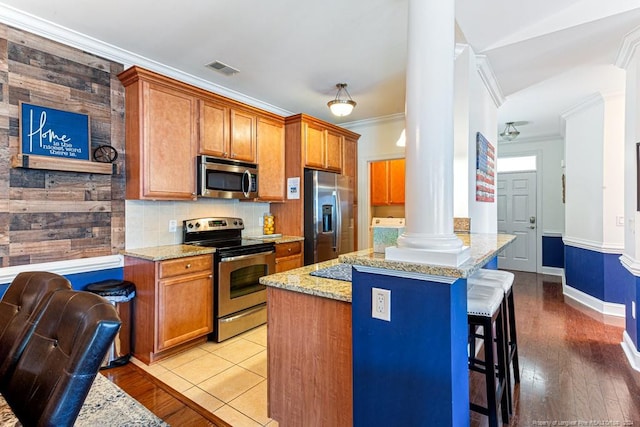 kitchen with a kitchen island, appliances with stainless steel finishes, a breakfast bar area, light wood-type flooring, and ornate columns