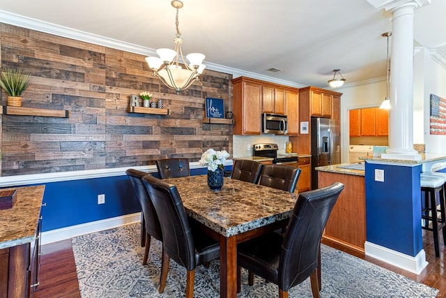 dining room with wooden walls, crown molding, decorative columns, an inviting chandelier, and dark hardwood / wood-style flooring