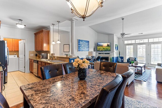 dining area featuring light hardwood / wood-style floors, ornate columns, washer / dryer, sink, and ceiling fan with notable chandelier