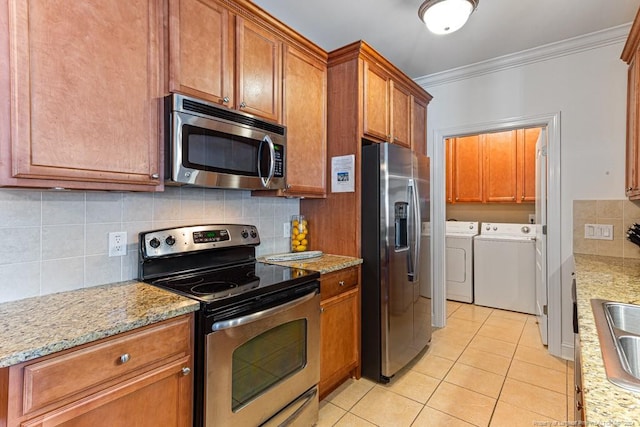 kitchen with appliances with stainless steel finishes, light stone countertops, separate washer and dryer, ornamental molding, and light tile patterned flooring