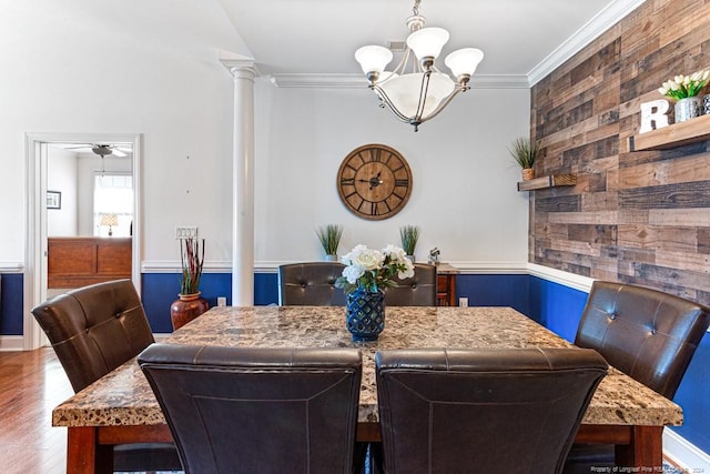 dining room with hardwood / wood-style floors, decorative columns, ornamental molding, ceiling fan with notable chandelier, and wooden walls