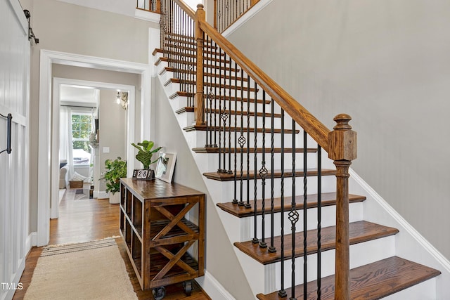 staircase featuring baseboards, a barn door, and wood finished floors