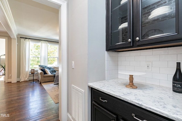 bar featuring dark wood-type flooring, light stone counters, decorative backsplash, and ornamental molding