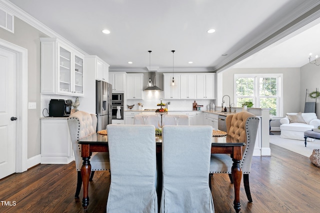 kitchen with wall chimney range hood, dark wood-type flooring, white cabinets, pendant lighting, and appliances with stainless steel finishes