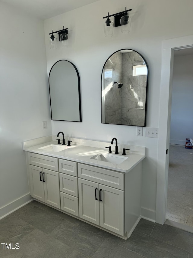 bathroom with double vanity, tiled shower, a sink, and baseboards