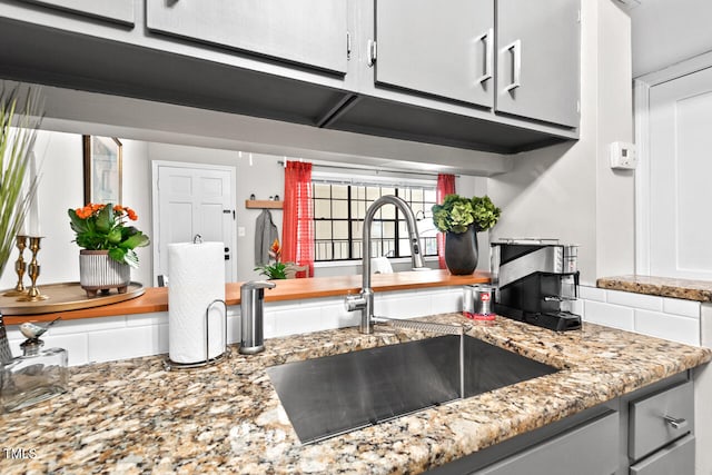 kitchen featuring light stone counters, white cabinetry, and sink