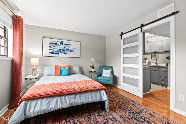 bedroom with a barn door, light hardwood / wood-style flooring, and sink