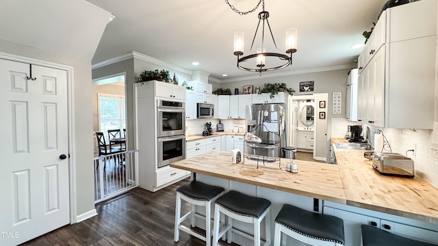 kitchen with white cabinets, appliances with stainless steel finishes, a kitchen breakfast bar, a chandelier, and butcher block counters