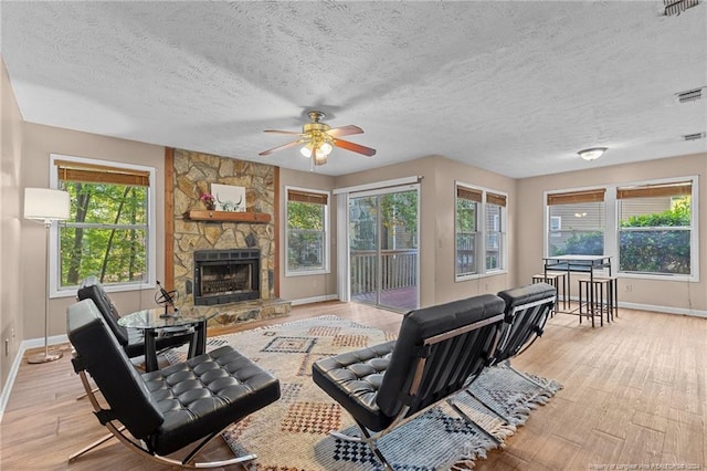 living room with a stone fireplace, light wood-type flooring, a textured ceiling, and ceiling fan