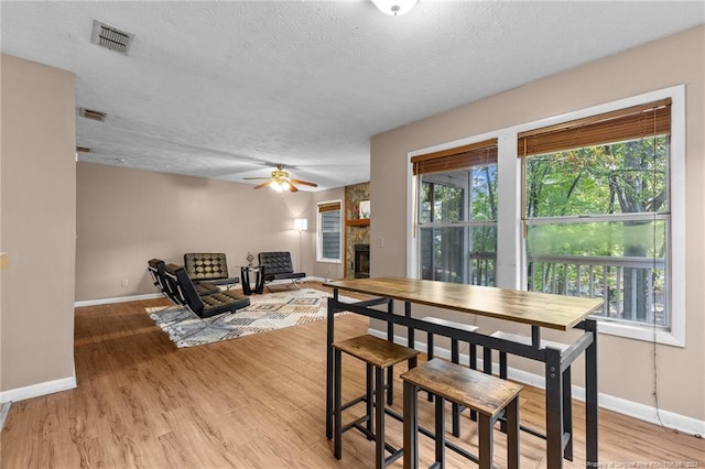 dining area featuring ceiling fan, a stone fireplace, a textured ceiling, and light hardwood / wood-style flooring