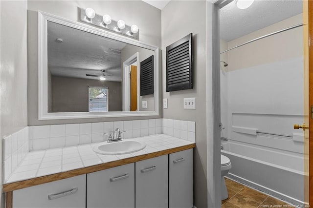 full bathroom featuring shower / washtub combination, toilet, a textured ceiling, vanity, and ceiling fan