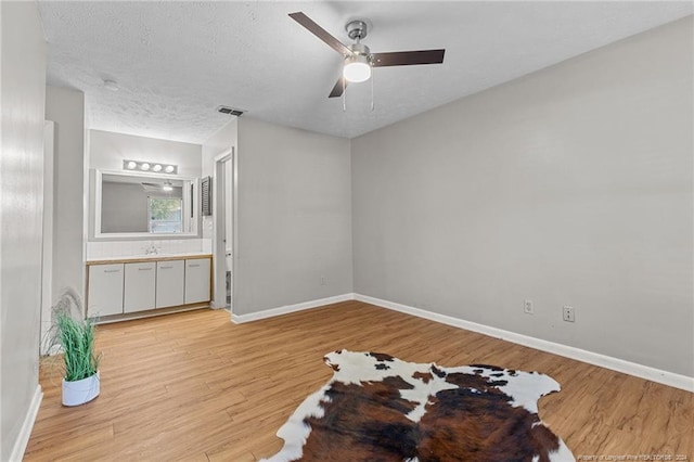 unfurnished bedroom with light hardwood / wood-style floors, ensuite bath, sink, ceiling fan, and a textured ceiling