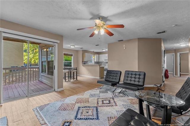 living room featuring light wood-type flooring, a textured ceiling, and ceiling fan