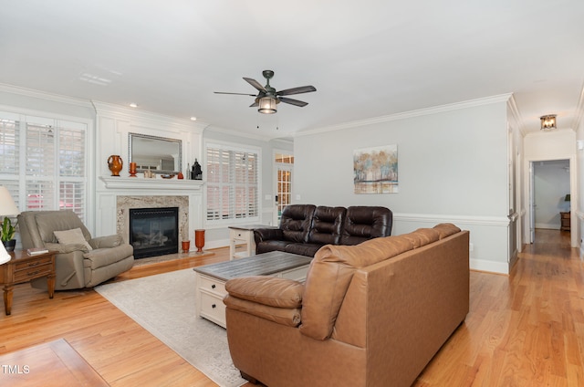 living room featuring crown molding, a fireplace, ceiling fan, and light wood-type flooring