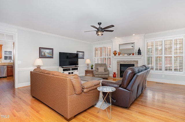 living room with a fireplace, light wood-type flooring, ceiling fan, and crown molding