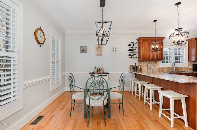 dining area featuring light wood-type flooring, a notable chandelier, ornamental molding, and sink