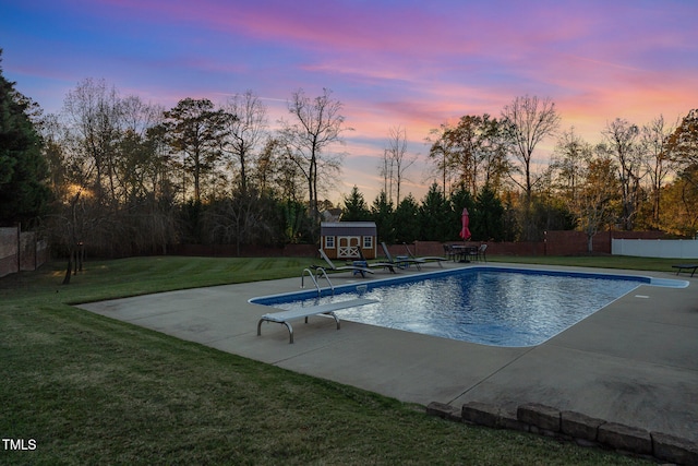 pool at dusk featuring a lawn, a patio area, a diving board, and a storage shed