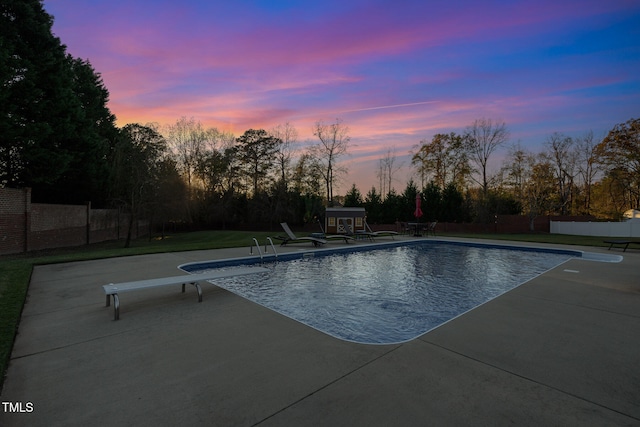 pool at dusk with a diving board, a yard, and a patio