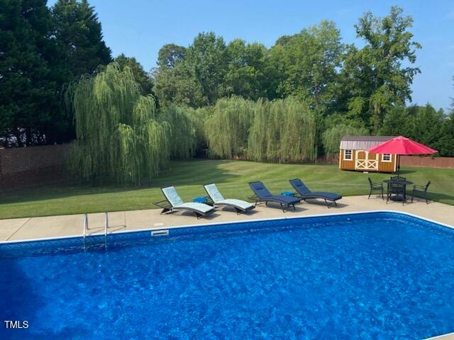 view of swimming pool featuring a lawn and a storage shed