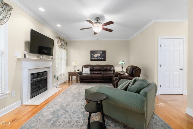 living room featuring a premium fireplace, light hardwood / wood-style flooring, ornamental molding, and ceiling fan