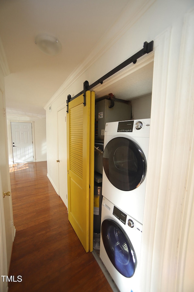 laundry room featuring dark wood-type flooring, stacked washer and clothes dryer, a barn door, and crown molding